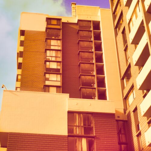 Looking up at an orange colored Gateview building with a blue sky background, from the Plaza.