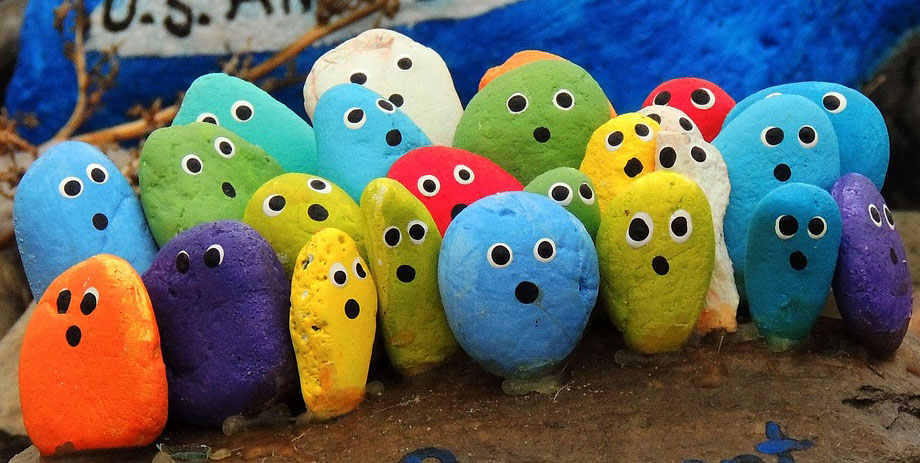Colorful, pebble-like figures with painted eyes and mouths are grouped together on a rock surface.